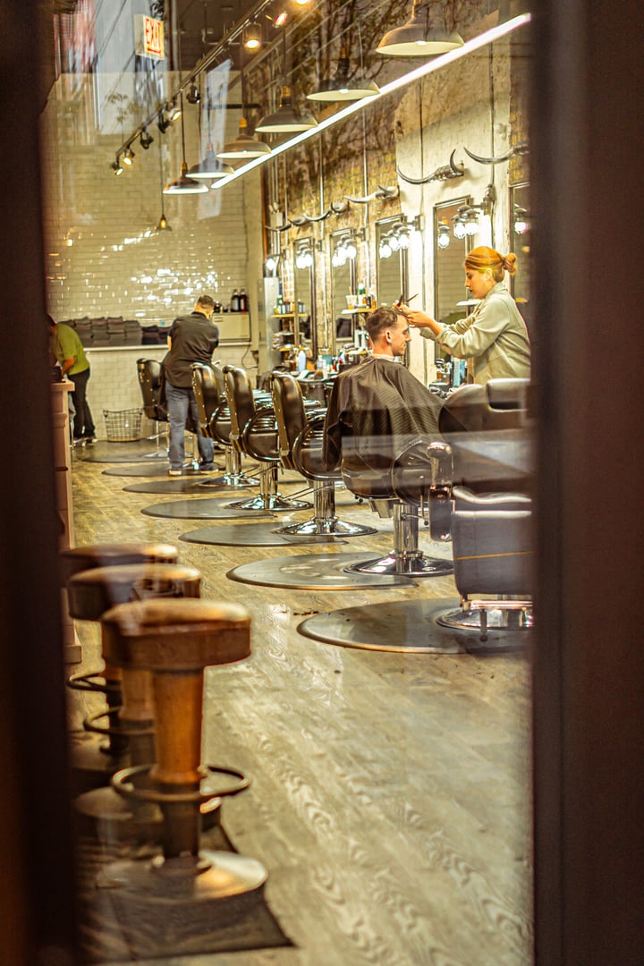 Chicago, United States – September 30, 2024: A glimpse inside a bustling barbershop, with customers seated in barber chairs and stylists at work, captured through a window.